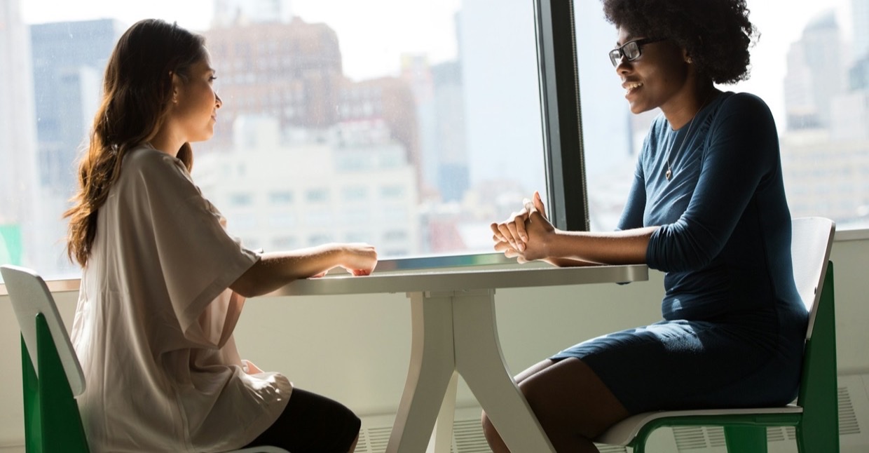 Twee vrouwen in gesprek aan een tafel bij het raam